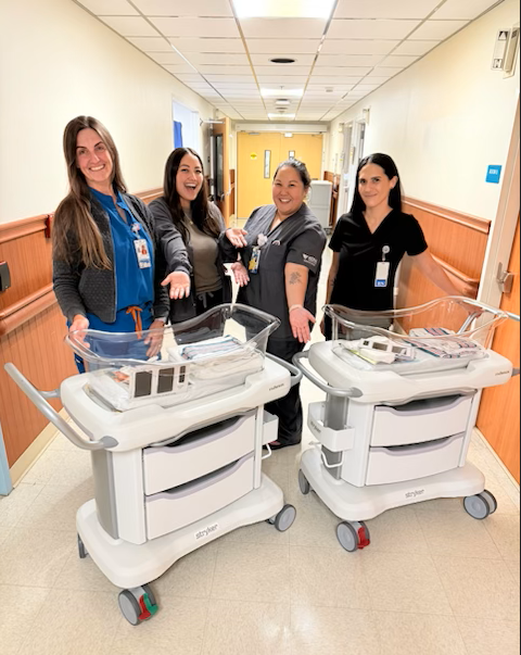 four nurses standing proudly behind two new baby bassinets.